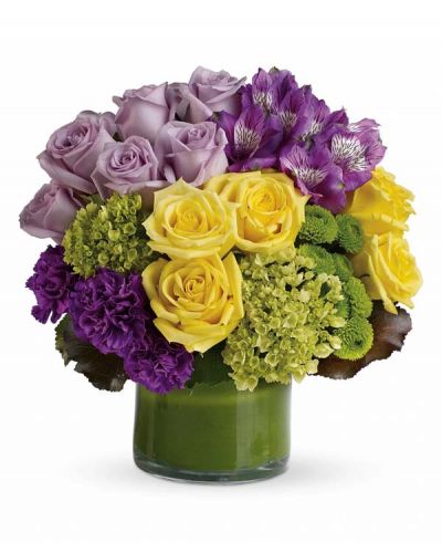 This chic arrangement of Purple Perfection includes miniature green hydrangea, lavender and yellow roses, purple alstroemeria, dark purple carnations, green button spray chrysanthemums, galax leaves and a ti leaf delivered in a clear glass vase.